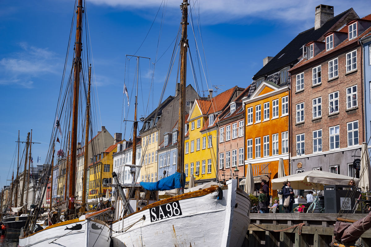 Vom Wasser aus betrachtet liegen die alten Segelschiffe der Fischer im Hafen von Nyhavn vor den bunten Fassaden der alten Handelshäuser.
