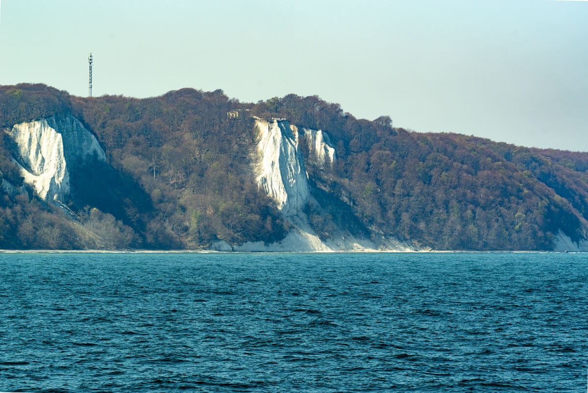 Vom Wasser aus sieht man die Küste von der Insel Rügen. Die weißen Kreidefelsen an der Steilküste die nicht von Bäumen bewachsen sind ragen hervor
