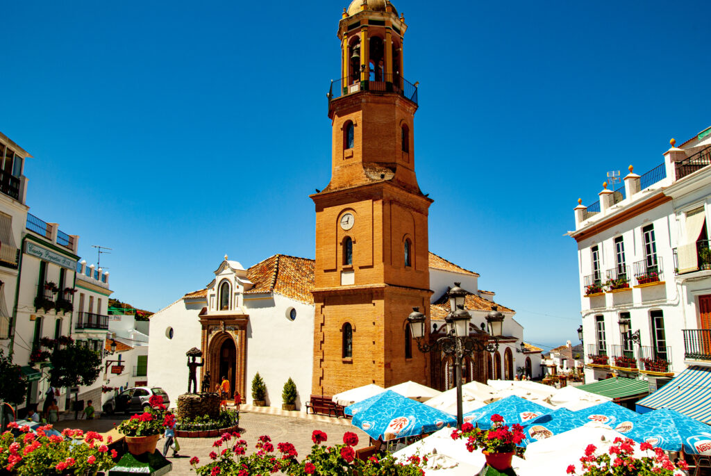 Weiße Häuser und ein blauer Himmel rahmen in der Mitte des Bildes die Kirche "Parroquia Nuestra Señora de la Asunción" ein.