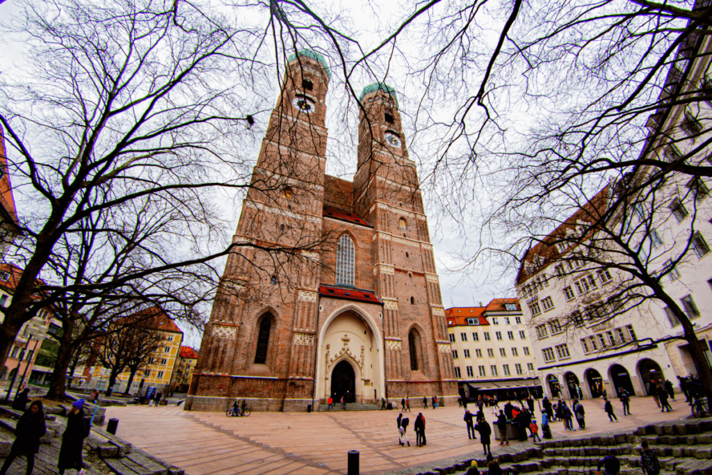 Vom Vorplatz hinauf blickend zu den Türmen der Frauenkirche. Die Backsteinfassade wird durch die kahlen Äste der nahe stehenden Bäume leicht verdeckt.