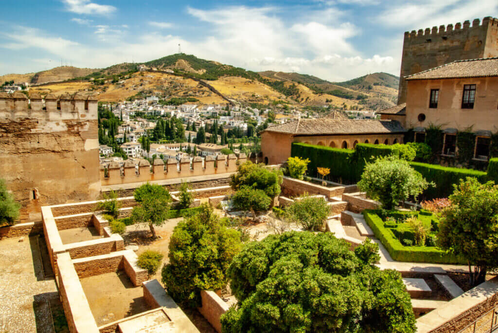 Eine Gartenanlage innerhalb der Stadtmauern. Hecken und kleine Bäume über die die Stadtmauer ragt und einen Blick auf die Stadt Granada zulässt.