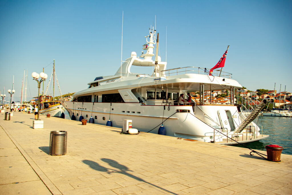 Die Bootsanlegestelle in Trogir. Zu sehen ist eine große Yacht die mit anderen Schiffen und Booten bei blauem Himmel und strahlendem Sonnenschein angelegt hat