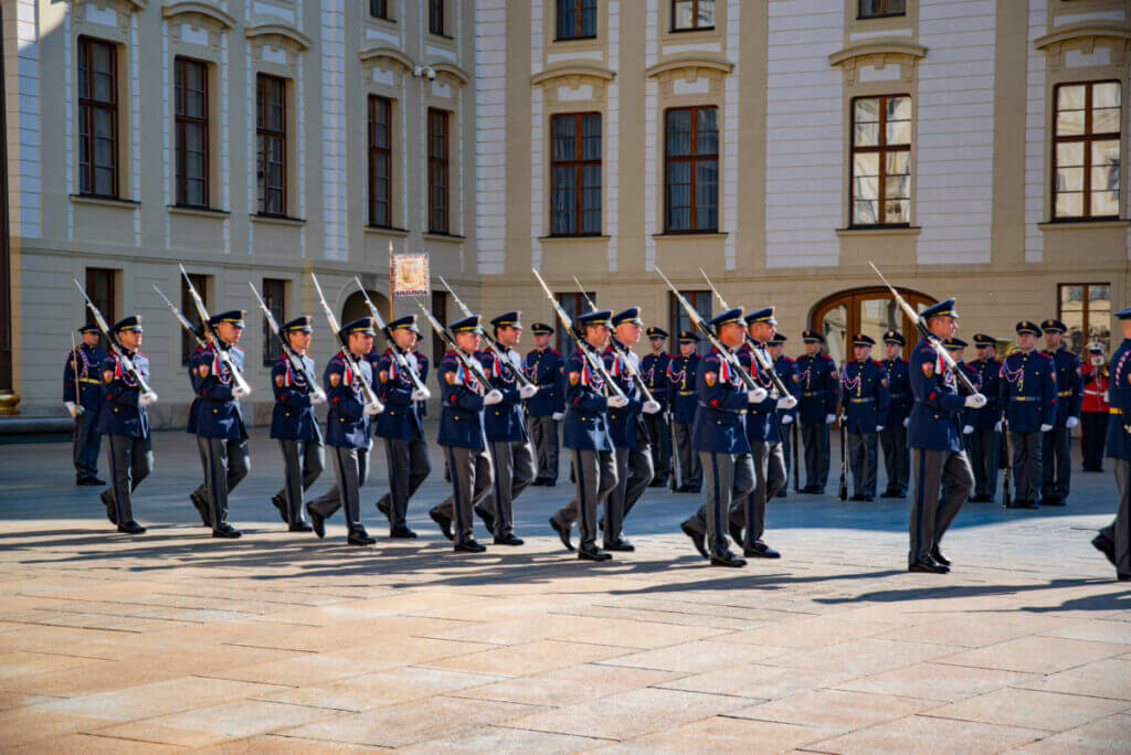Die Wachablösung auf einem Vorplatz der Prager Burg mit zahlreichen im gleichschritt maschierenden Soldaten in Schmuckuniform.