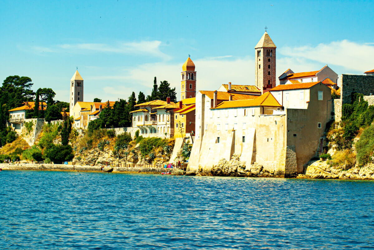 Vom Wasser der Adria aus erblickt man die alten Stadtmauern, die hoch am Ufer herausragen. Drei Türme ragen in der Altstadt heraus.