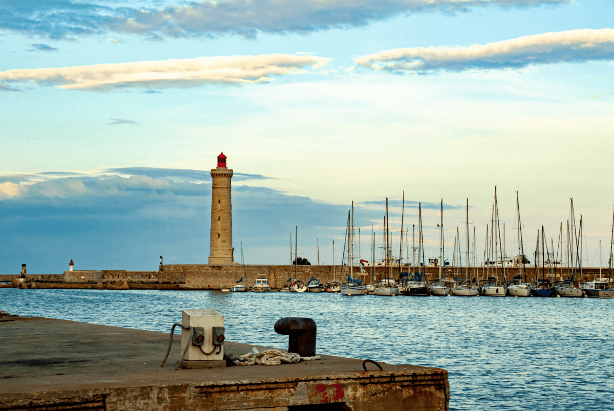 Das Hafenbecker der Stadt Sète bei abendlichem Licht. In der Bildmitte steht der Leuchtturm Saint-Louis mit einer roten Spitze
