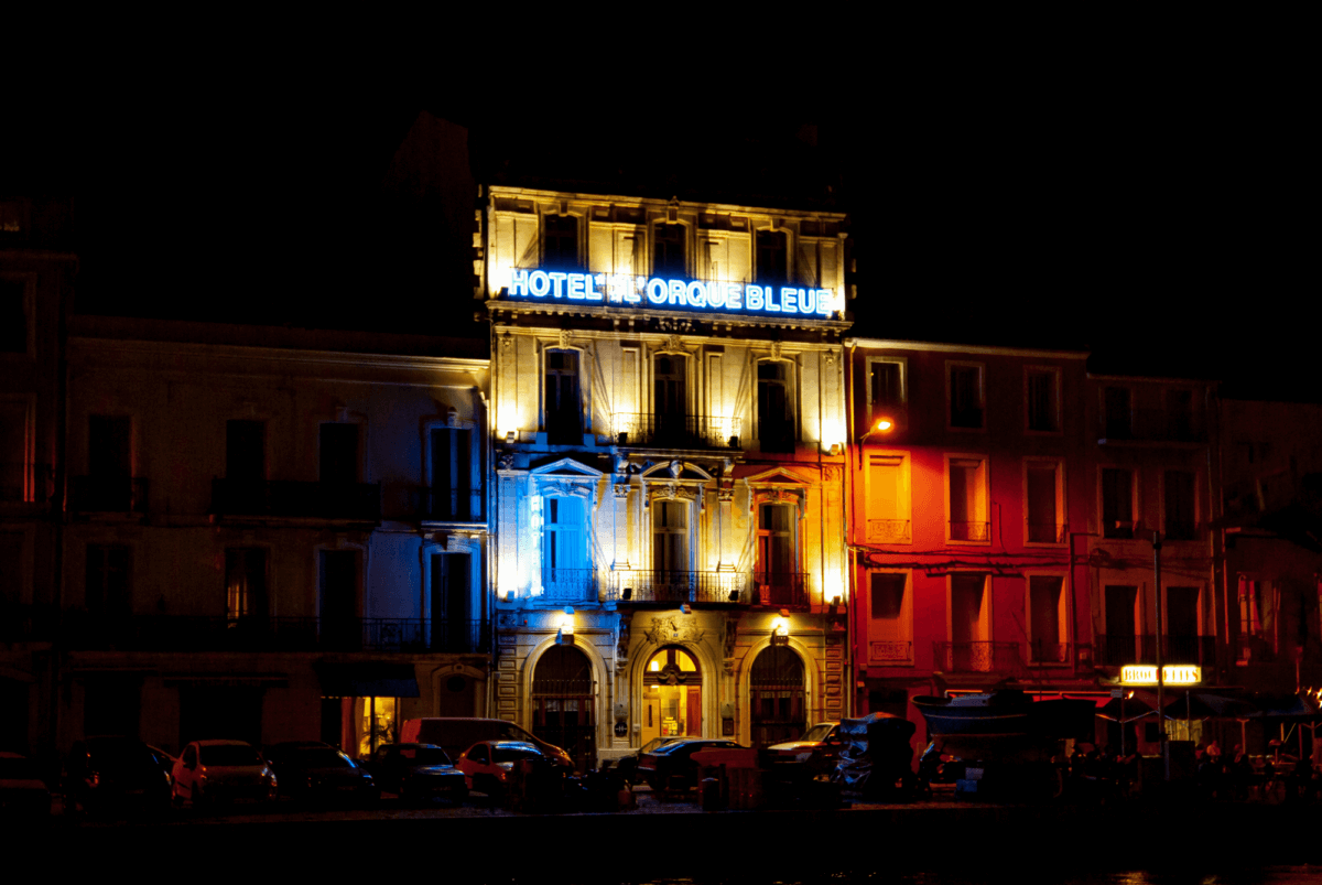 Eine Nachtaufnahme von der Hotelfassade des Hôtel l'Orque Bleue. Sie ist in den Farben blau, weiß und rot angeleuchtet. Es gehört zu den Unterkünfte, die mir gefallen