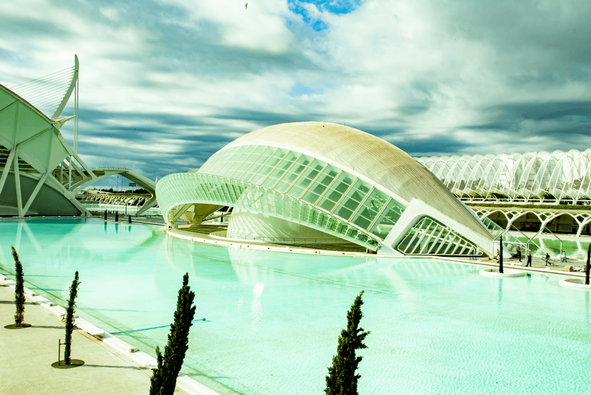 Ein futuristischer Neubau aus weißem Stahlbeton und Glas umgeben von einem flachen Wasserbecken schimmert das Gebäude türkisfarben.