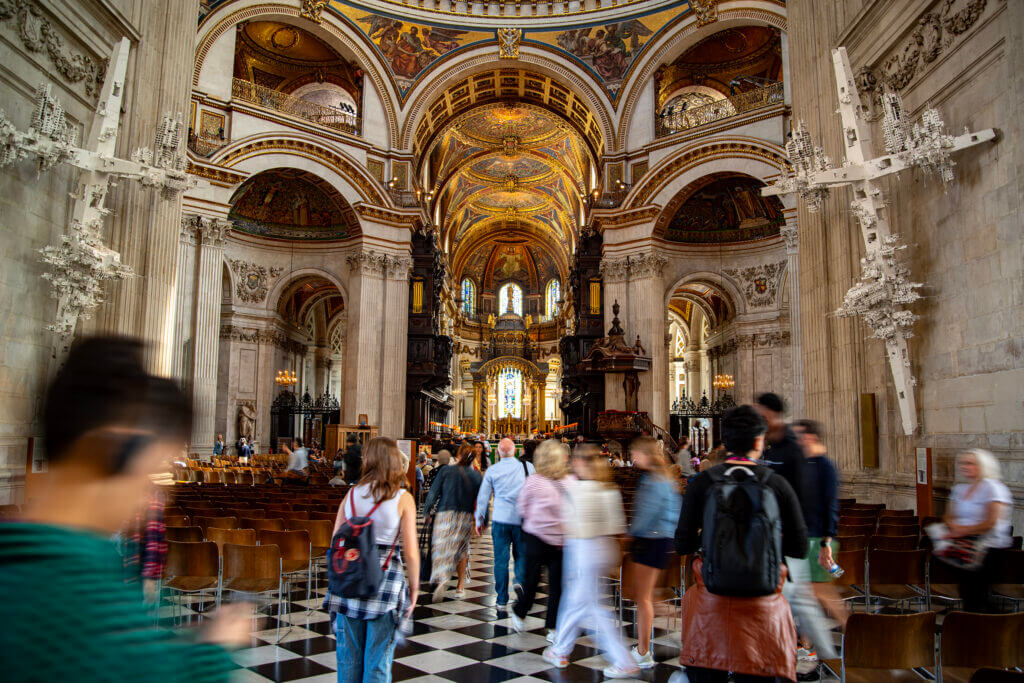 Im Inneren der Saint Pauls Cathedral sind zahlreiche Menschen versammelt, die die Architektur bewundern. Die Wände bestehen aus hellem Marmor und die Decken sind mit viel Gold geschmückz.