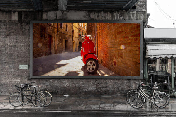 In den Gassen Sienas zwischen gemauerten Fassaden steht einsam eine rote Vespa. Das Bild ist als Poster ausgedruckt.