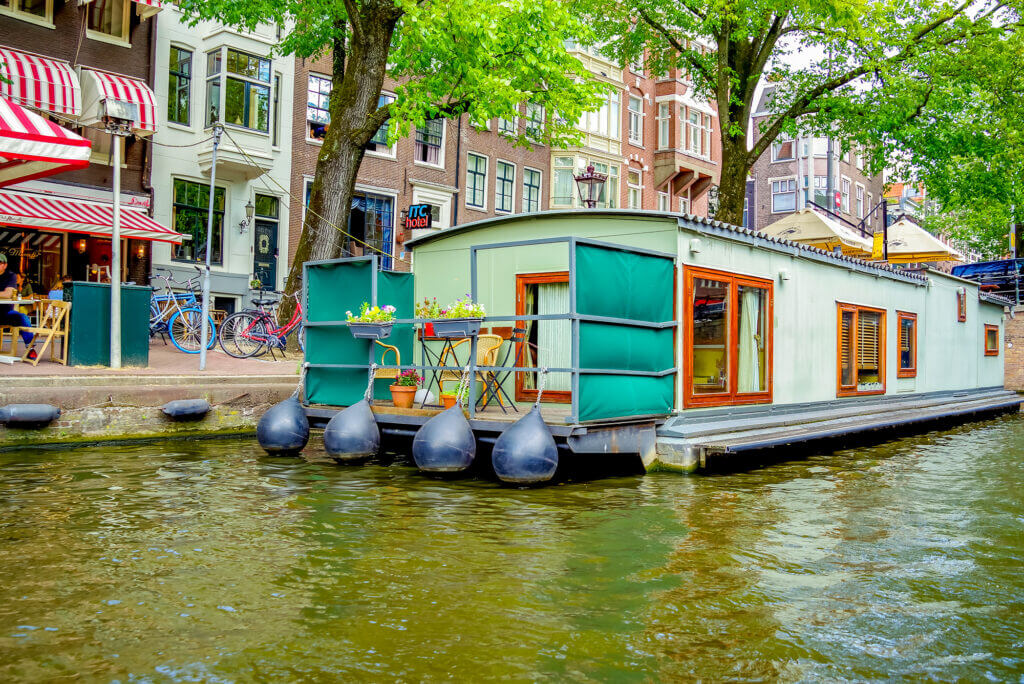 Ein Hausboot in den Kanälen von Amsterdam mit Terrasse und grünen Sichtschutzwänden