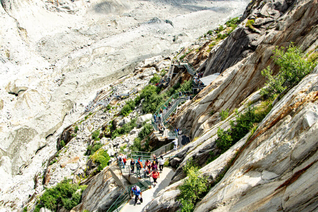 Das tiefe Tal des Mer de Glaces im Sommer. Besucher laufen den treppenreichen Weg hinuter zur Gletscherzunge.