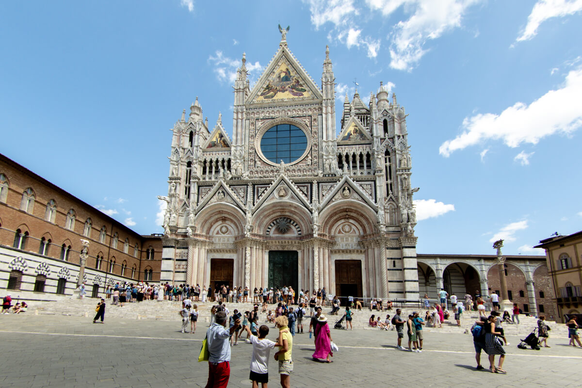 Der Vorplatz der Kathedrale von Siena ist mit vielen Menschen bevökert und bietet einen wunderbaren Blick auf das Eingangsportal des Gotteshauses