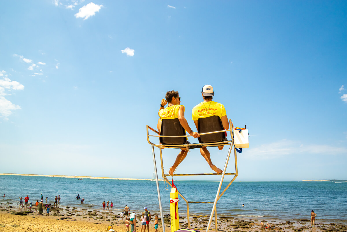 Rettungsschwimmer sitzen auf einem Hochsitz und beobachten den Strand, Sie tragen gelbe T-Shirts.