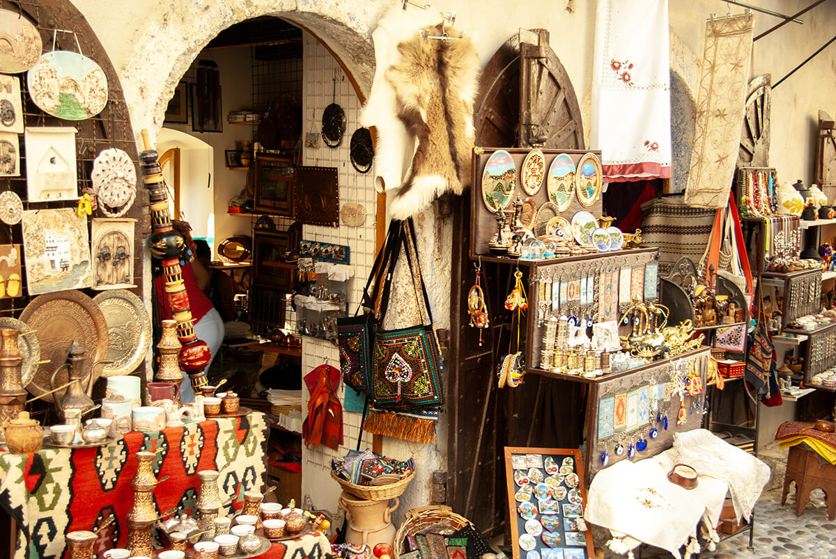 Ein typischer Souvenirladen in einer kleinen Gasse, Tierfelle, Kupferteller, Mokkatassen, bestickte Taschen stehen vor einem Laden zur Ansicht bereit.