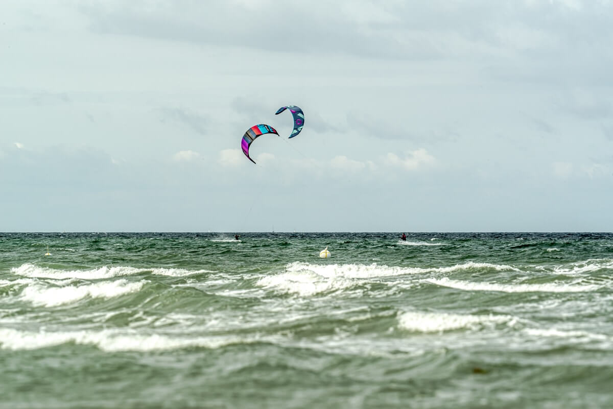 Wellenkämme auf der Ostsee auf der zwei Kitesurfer im Wasser surfen.