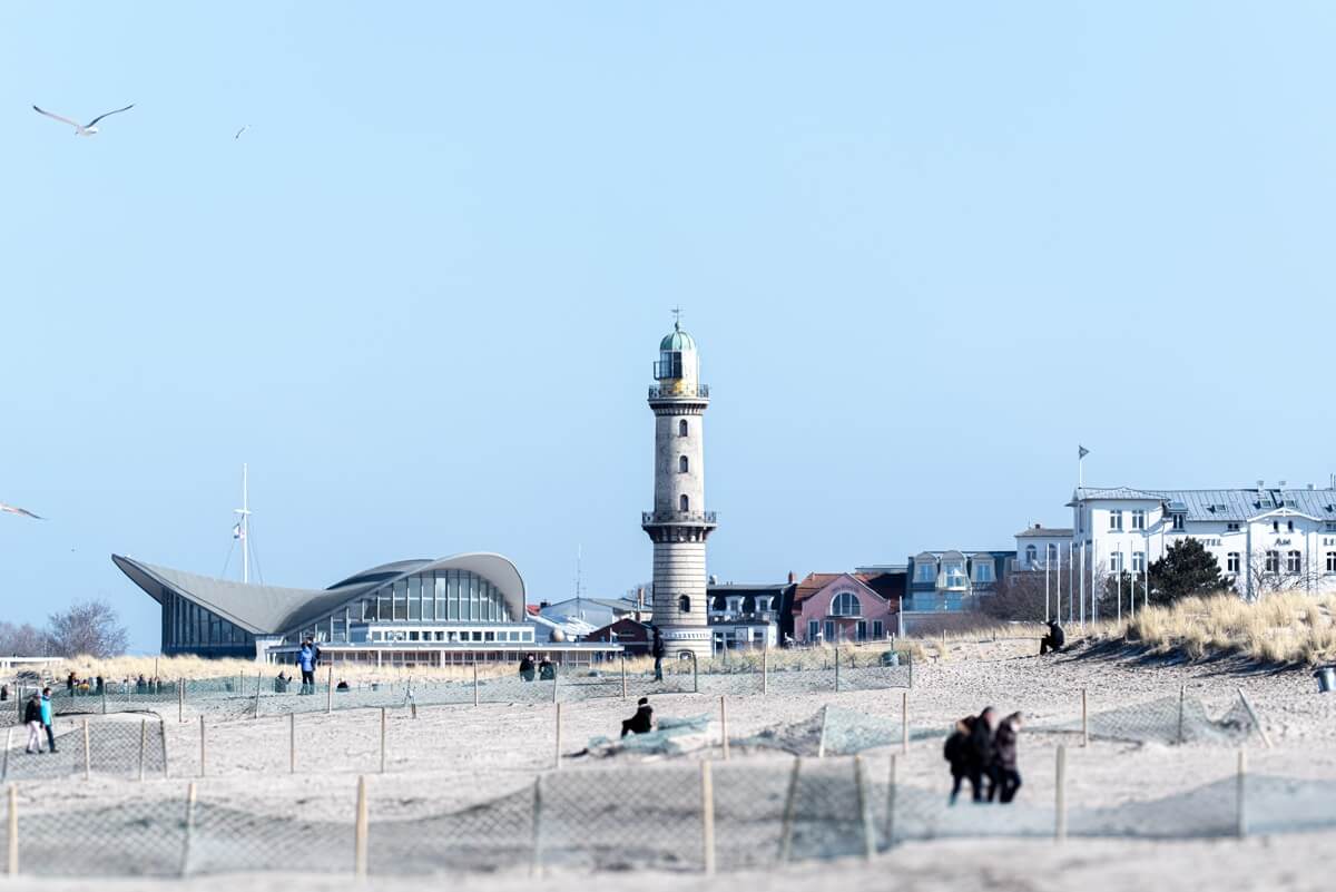 Ein breiter Sandstrand mit Dünenzäunen mit Blick auf den im Hintergrund stehenden Leuchtturm von Warnemünde