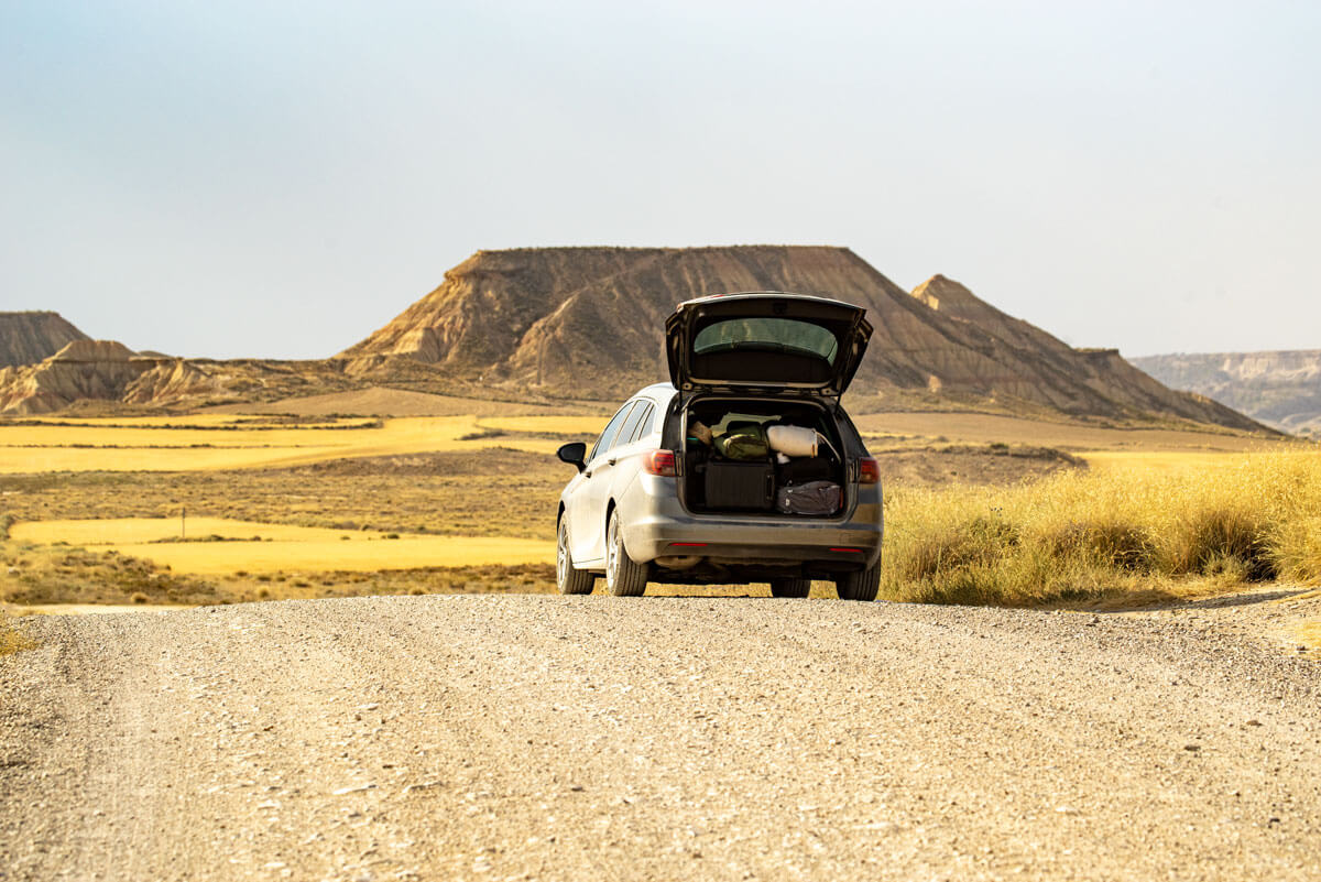 Von einer Straße in der Halbwüste aus erblickt man die weite Landschaft mit einem Tafelberg im Hintergrund. Dazwischen steht ein Auto mit offener Heckklappe.