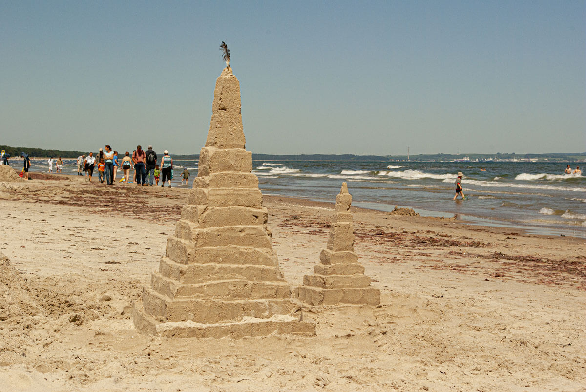 Eine Pyramide aus Sand am Strand. Im Hintergrund sieht man das Meer und die Wellen.