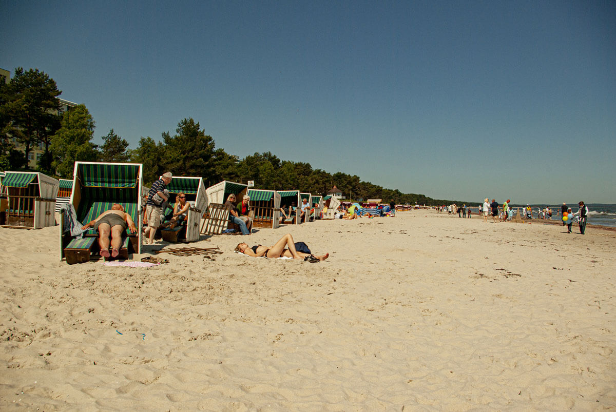 Ein feiner Sandstrand mit einigen Strandkörben, in denen Menschen sich viel Zeit nehmen.