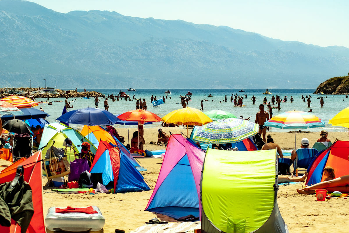 Lopars größter Strand in einer großen Bucht und einem Sandstrand an dessen Ufer unzählige bunte Sonnenschirme und Sonnenzelte stehen.