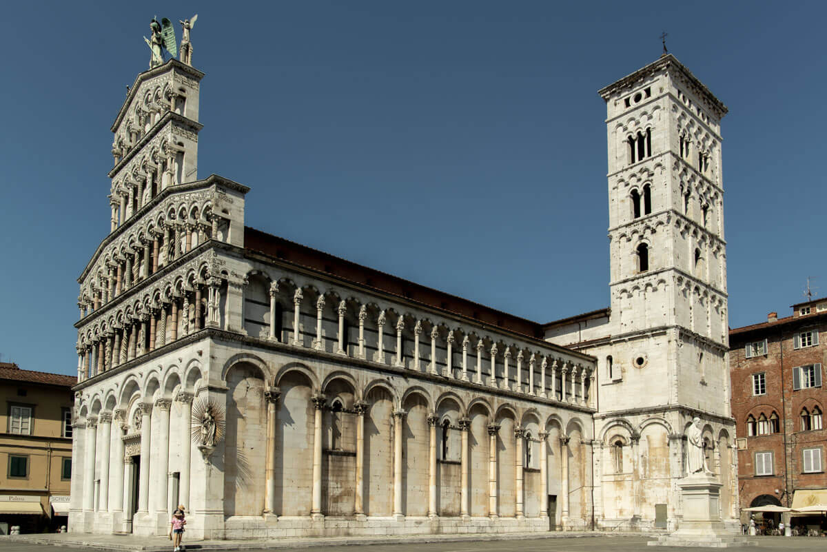 Zu sehen ist eine Kathedrale in Lucca, die aus weißen Marmor erbaut wurde. Links befindet sich das Eingangsportal und rechts der Turm der Kathedrale.