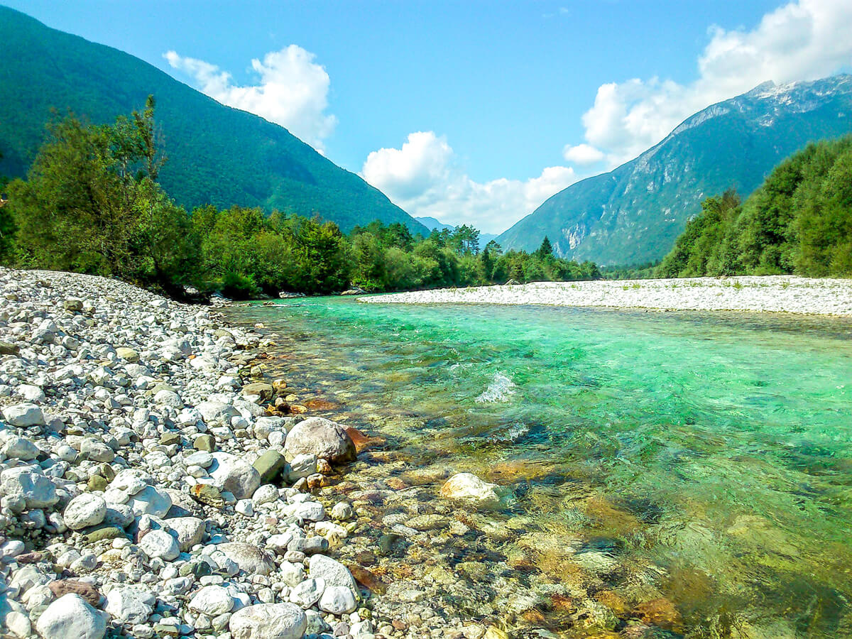 Ein flacher Bachlauf eines Flusses wird von steinigen Ufer und dichten Wäldern gesäumen.