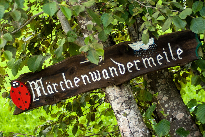 Ein Hinweisschild aus Holz und der Aufschrift Märchenwandermeile und einen roten Marienkäfer
