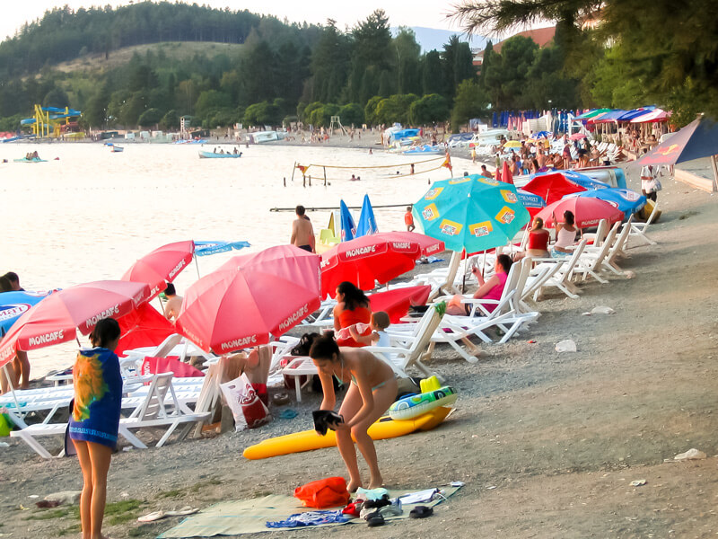 Ein Strand am Ohridsee mit zahlreichen Badegästen. Sonnenschirme und Liegen säumen den Strand.