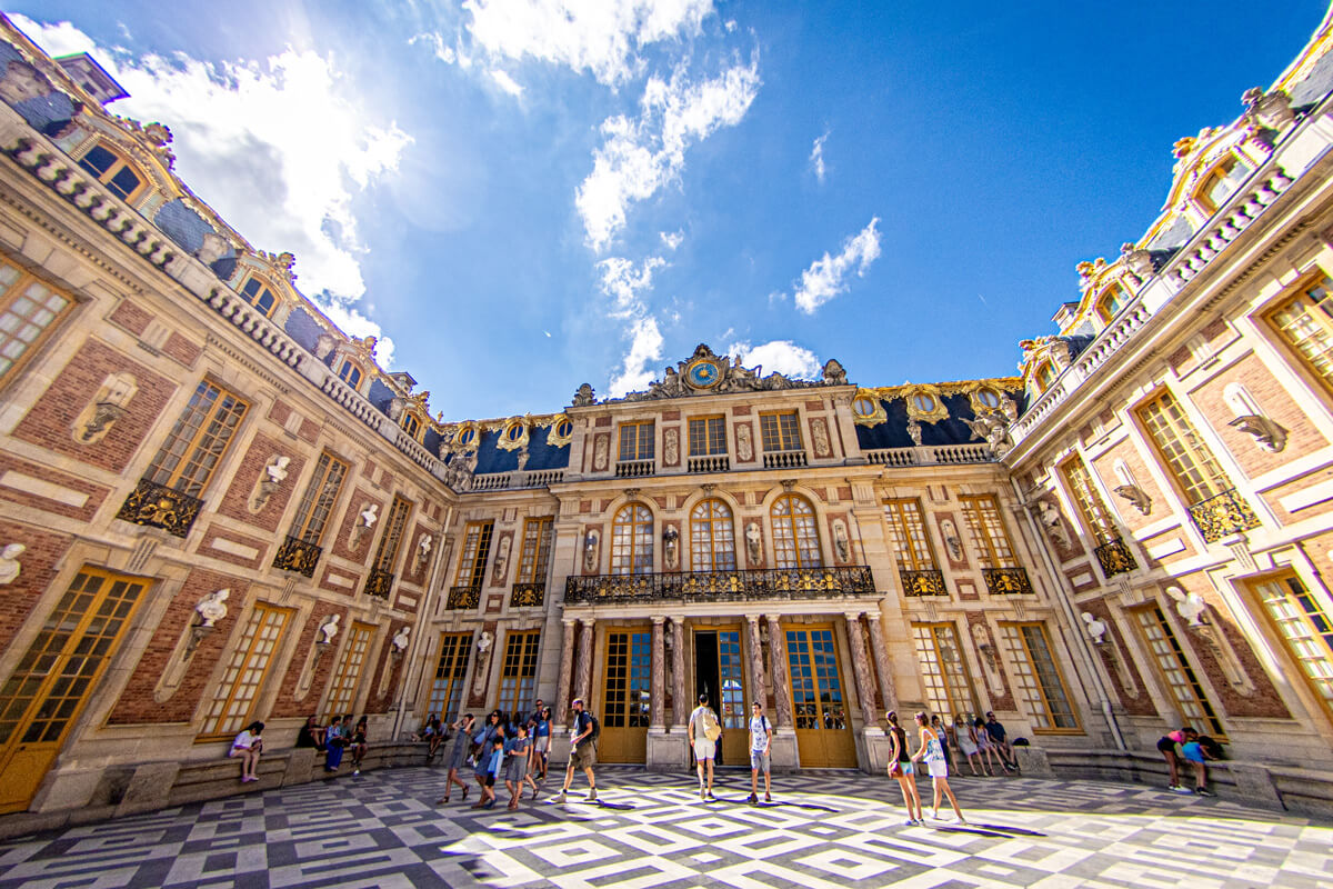 Ein Drei-Seiten-Hof des Schlosses in Versailles mit prachtvollen Fassaden geschmückt mit goldenen Verzierungen und einen Boden aus Marmor.